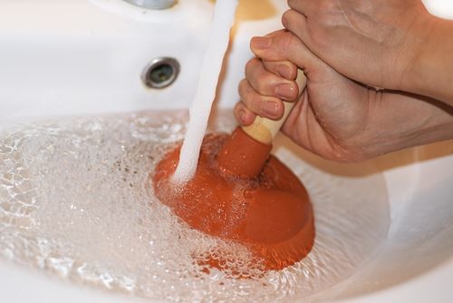 A person using a plunger on a clogged sink drain.
